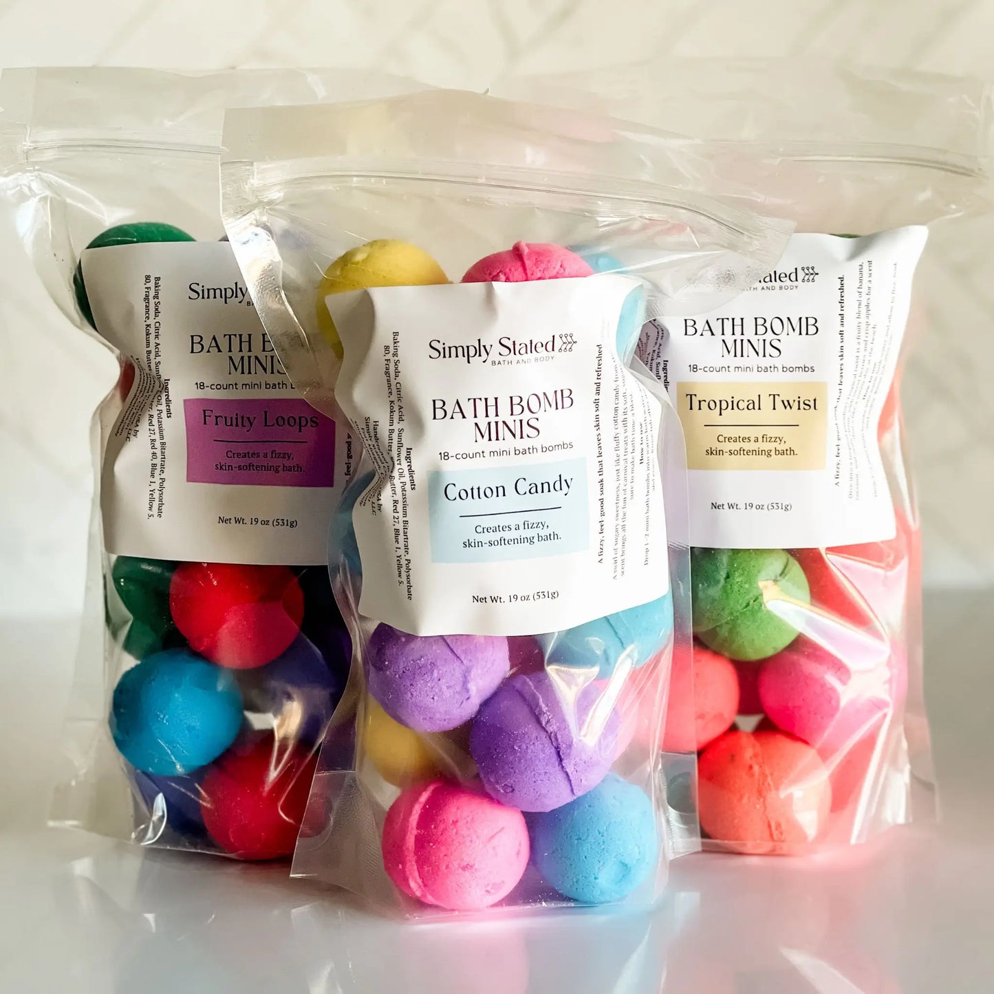 Three bags of bath bomb minis with colorful bombs inside, labeled 'Fruity Loop', 'Cotton Candy', and 'Tropical Twist'.
