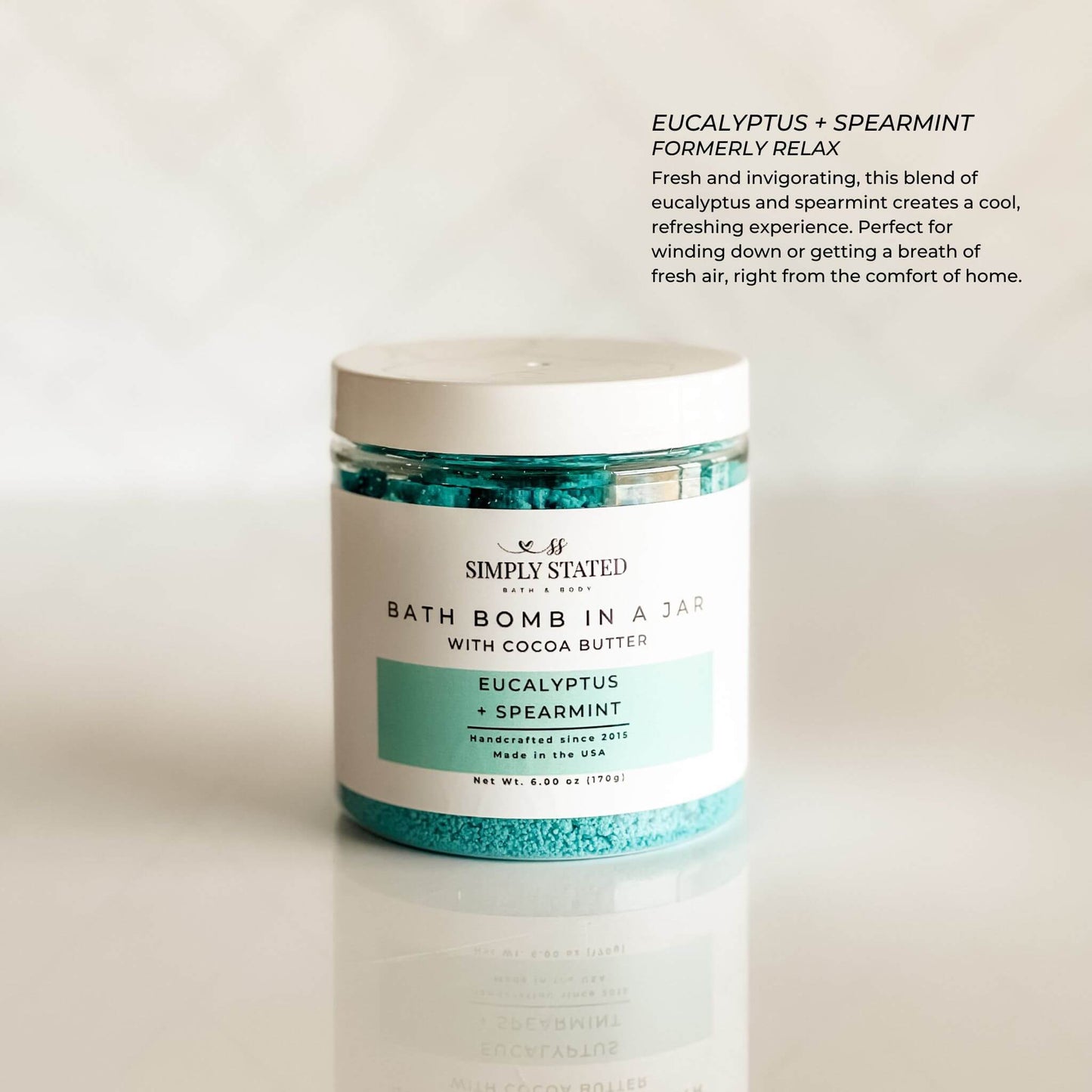 Aromatherapy bath bomb in a jar featuring the Eucalyptus + Spearmint blend. A refreshing mix of cool mint and invigorating eucalyptus for a spa-like self-care experience. Packaged in a clear jar with a minimalist label, highlighting its premium bath soak formula with cocoa butter for skin nourishment.