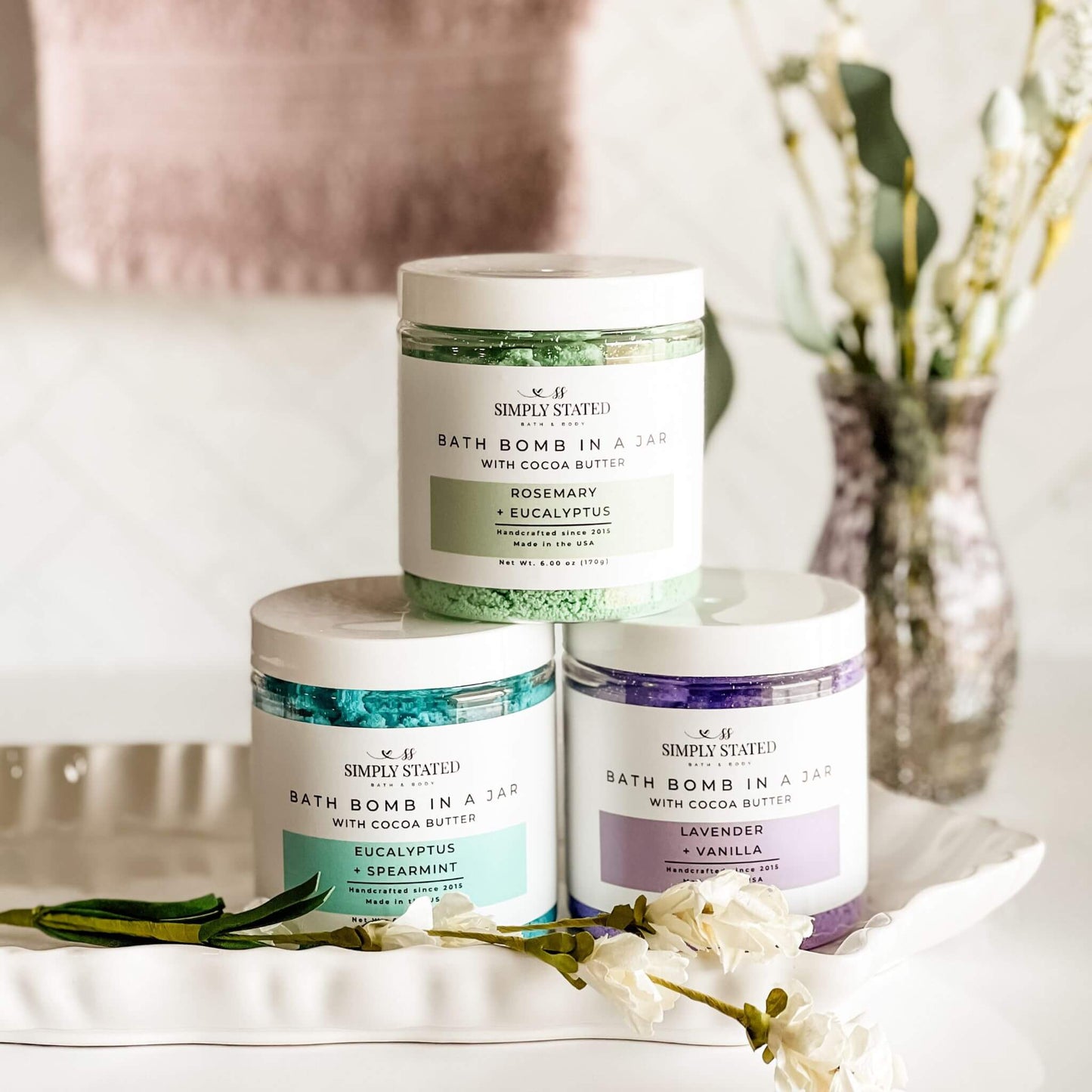 Simply Stated Bath & Body’s Aromatherapy Bath Bomb in a Jar collection, featuring three scents: Eucalyptus + Spearmint, Lavender + Vanilla, and Rosemary + Eucalyptus. Beautifully displayed in a spa-like setting with a soft, neutral aesthetic to emphasize relaxation and luxury self-care.