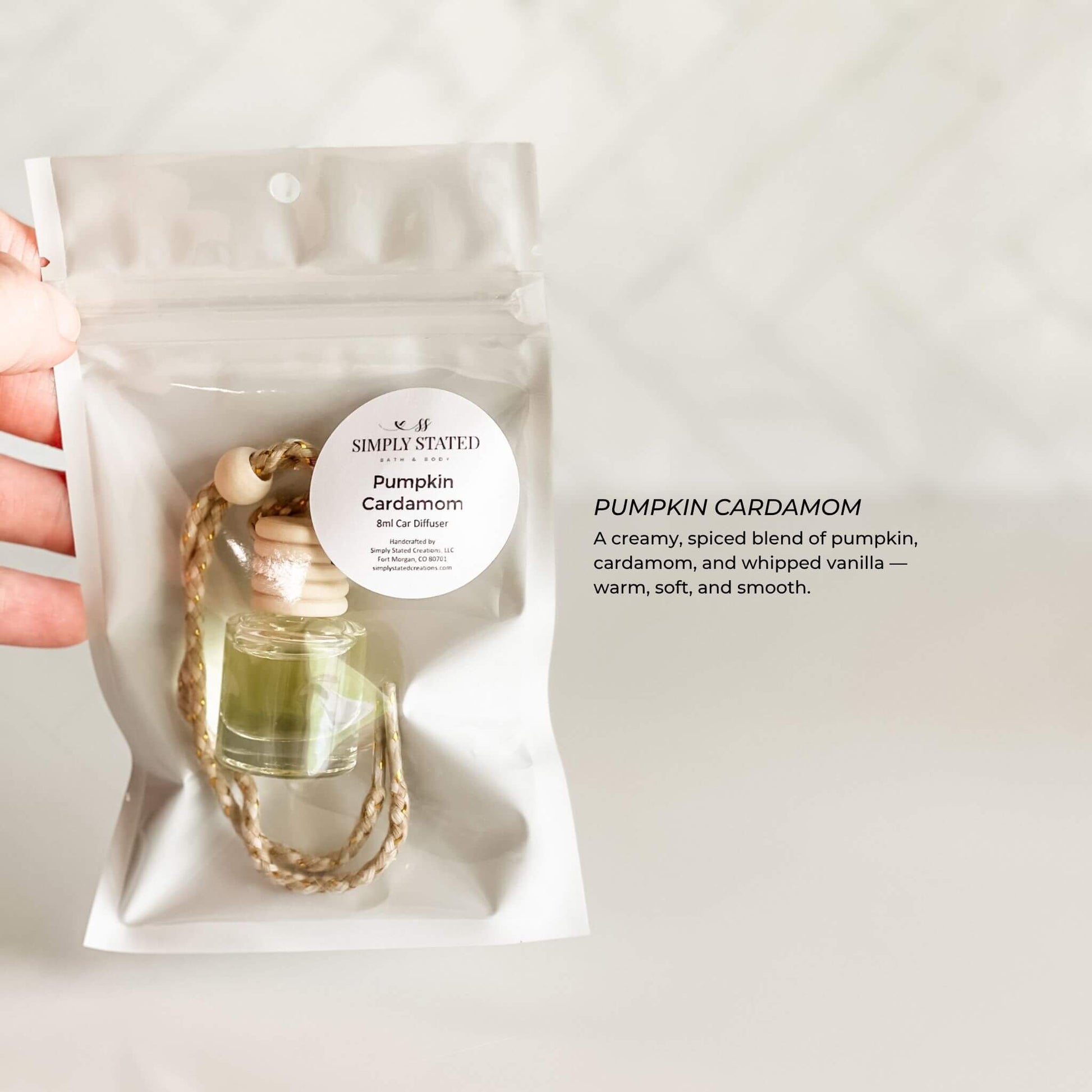 Hand holding a pumpkin cardamom diffuser with packaging on a light background