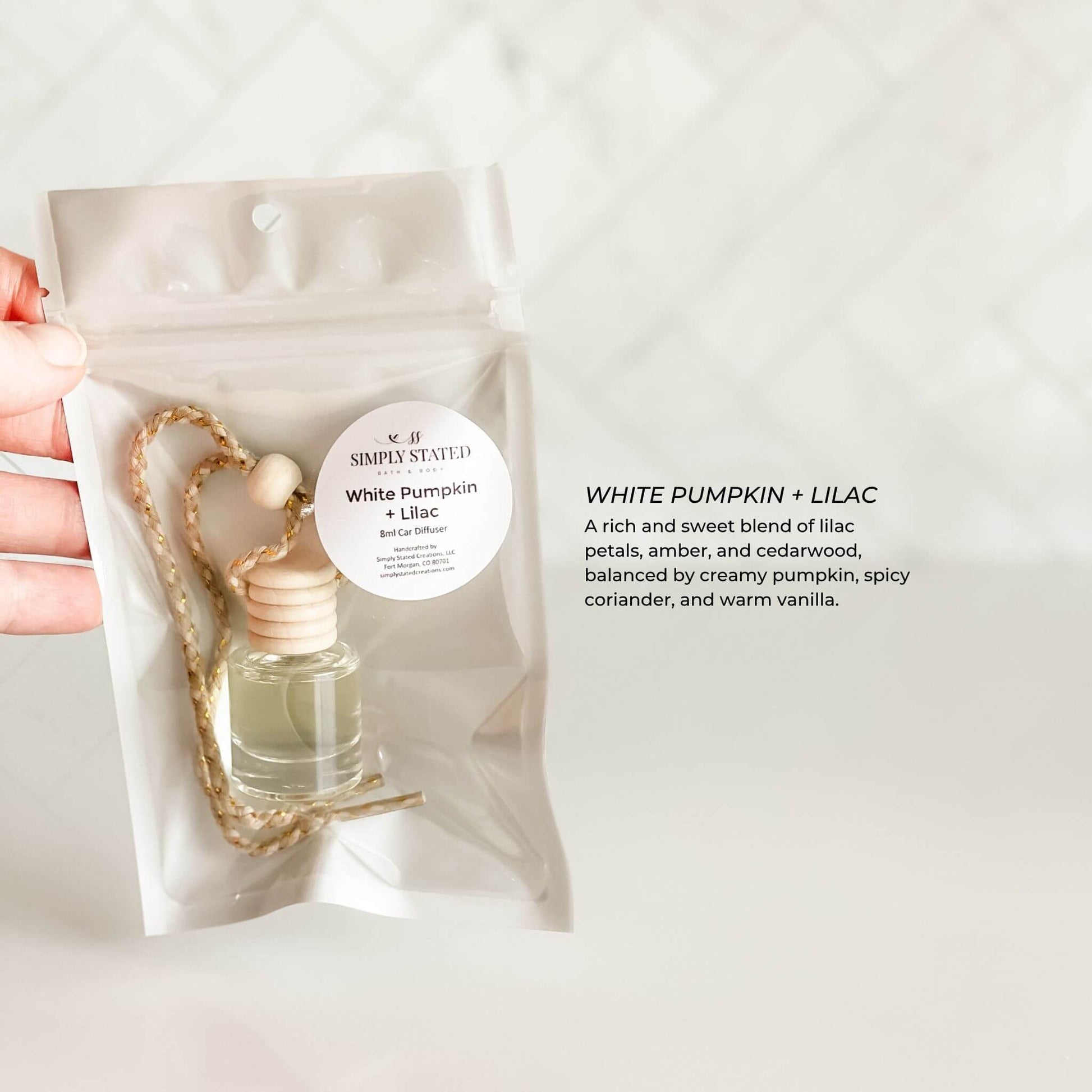 Hand holding a white pumpkin and lilac scented product packaging with a label.