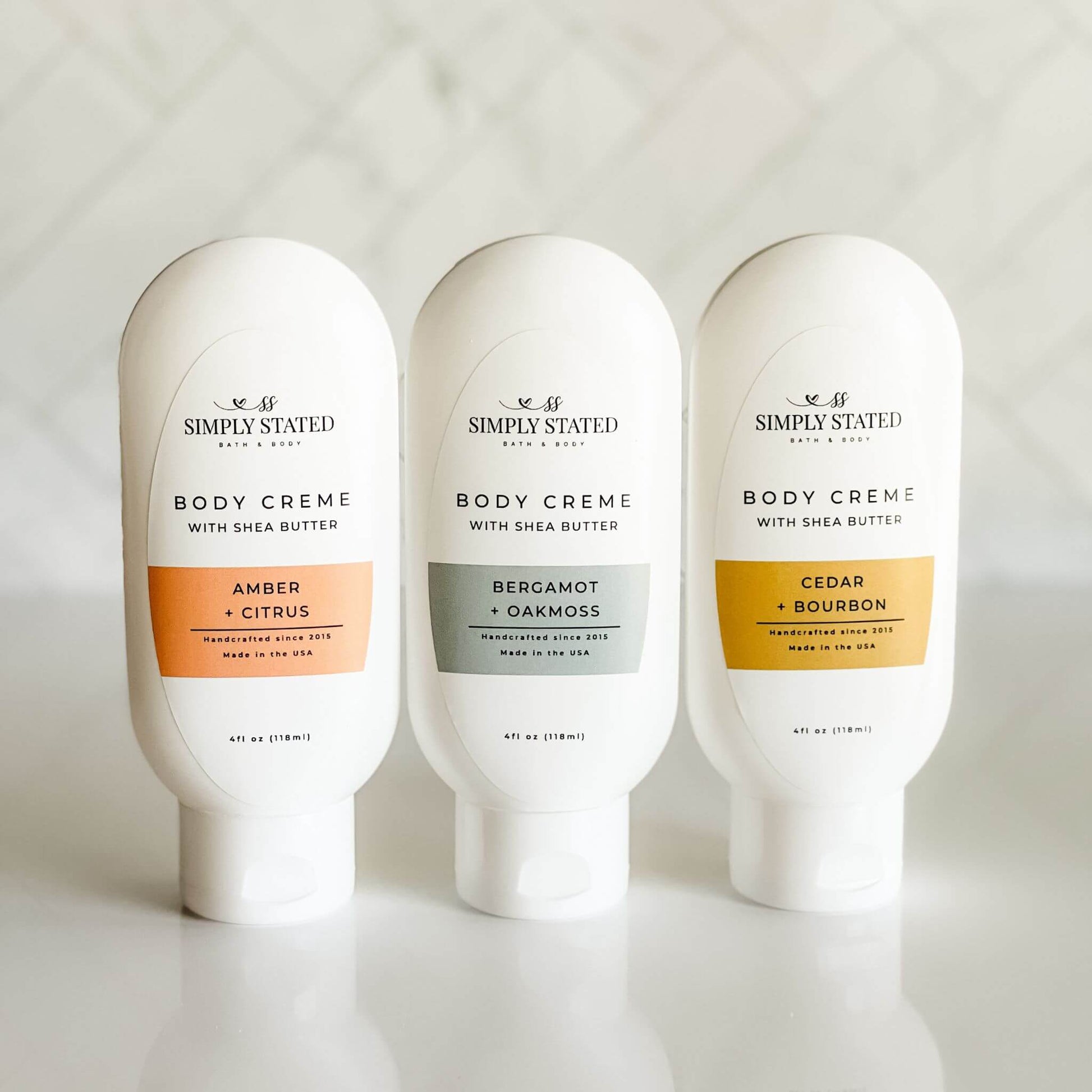 Group of 4 oz men's body creme bottles in three scents: Amber + Citrus, Bergamot + Oakmoss, and Cedar + Bourbon.