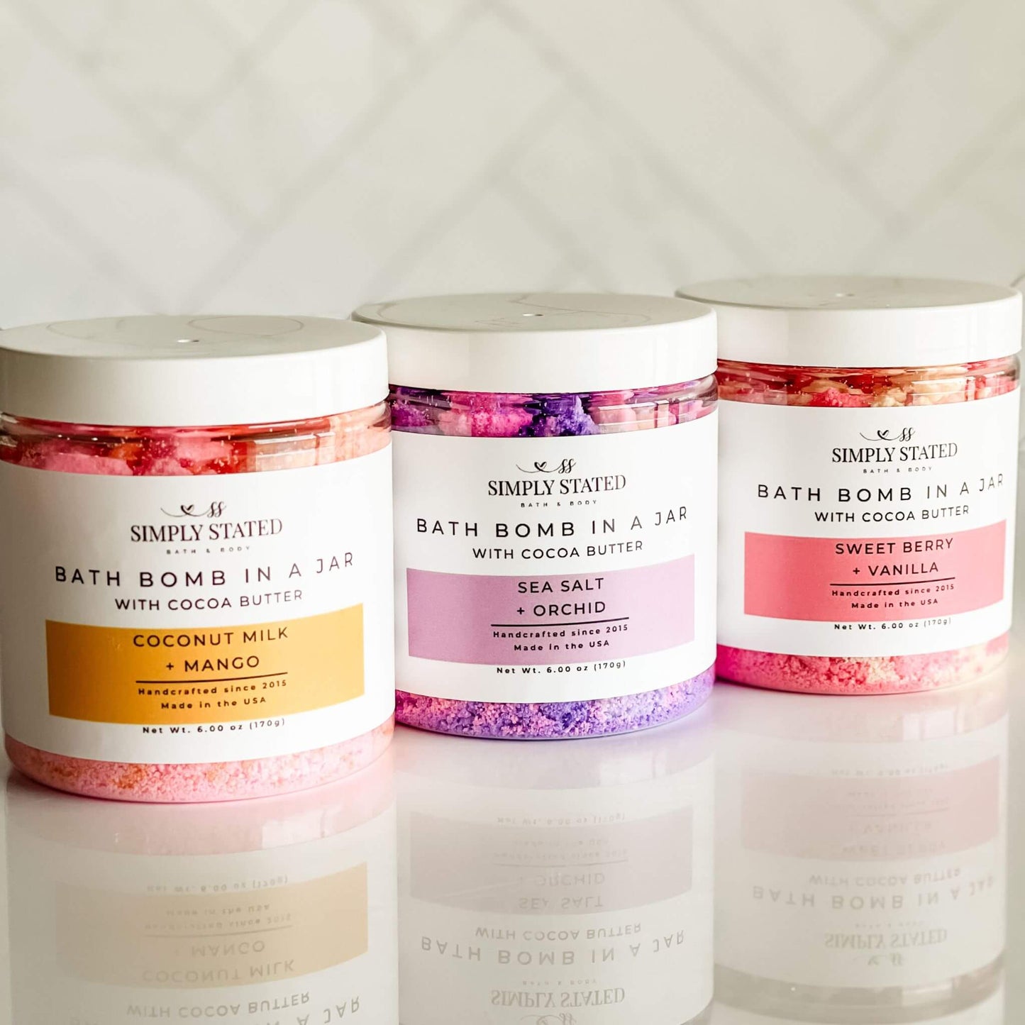 Simply Stated Bath & Body Signature Line Bath Bomb in a Jar collection featuring Coconut Milk + Mango, Sea Salt + Orchid, and Sweet Berry + Vanilla. A luxurious bath bomb powder made with cocoa butter and organic oils for a nourishing, skin-softening soak.