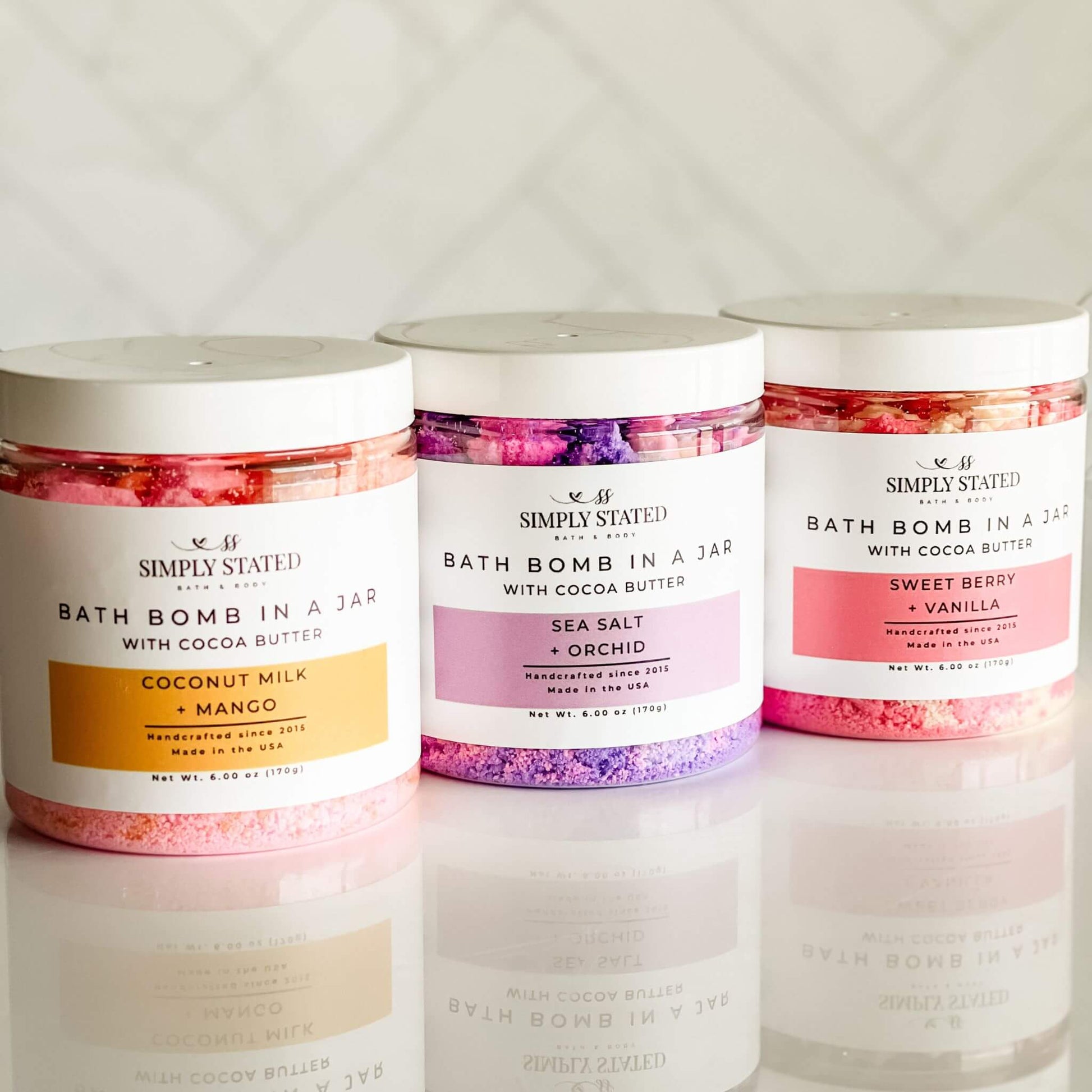 Simply Stated Bath & Body Signature Line Bath Bomb in a Jar collection featuring Coconut Milk + Mango, Sea Salt + Orchid, and Sweet Berry + Vanilla. A luxurious bath bomb powder made with cocoa butter and organic oils for a nourishing, skin-softening soak.