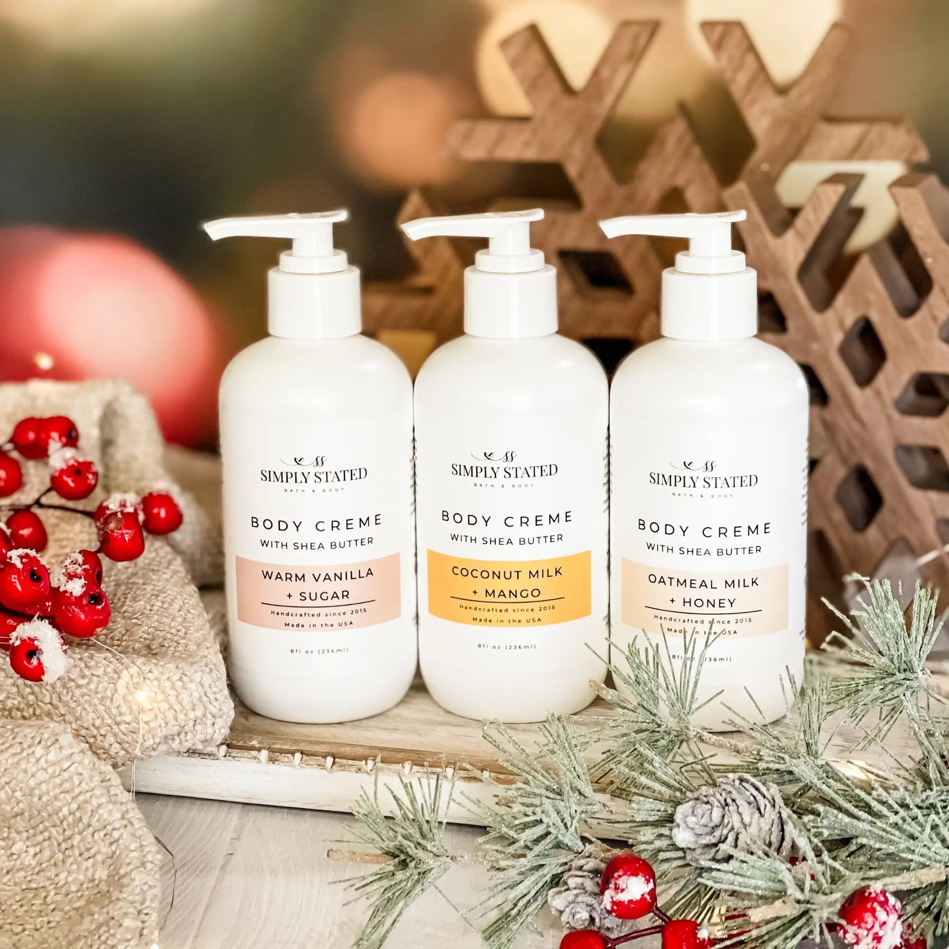 Three bottles of 'Simply Stated' body cream with Christmas decorations in the background