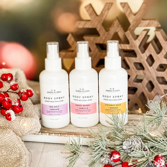 Three body spray bottles with different scents on a decorative background with Christmas elements.