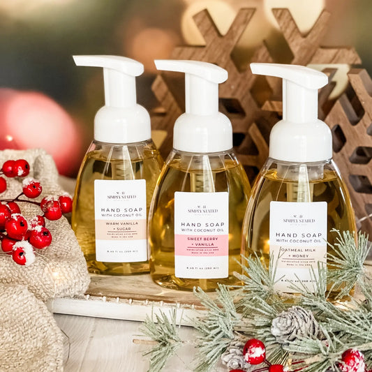 Three bottles of hand soap with pump dispensers on a decorative surface with Christmas elements.