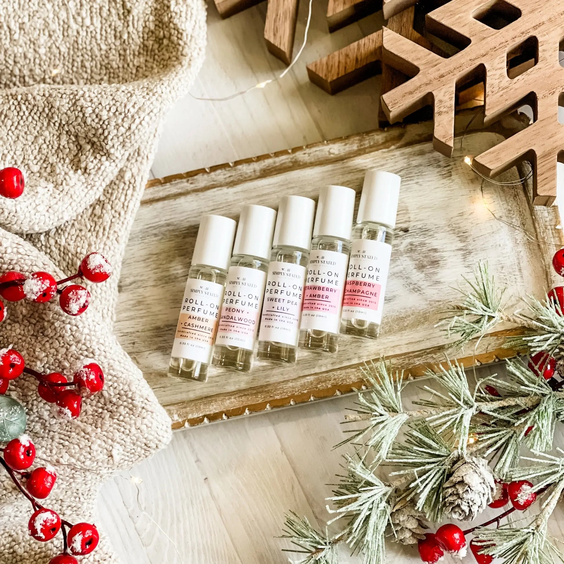 Five small perfume bottles on a wooden tray with Christmas decorations.