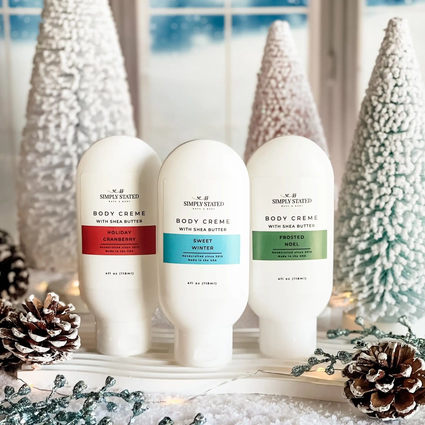 Three bottles of Simply Stated Body Creme with Christmas decorations in the background