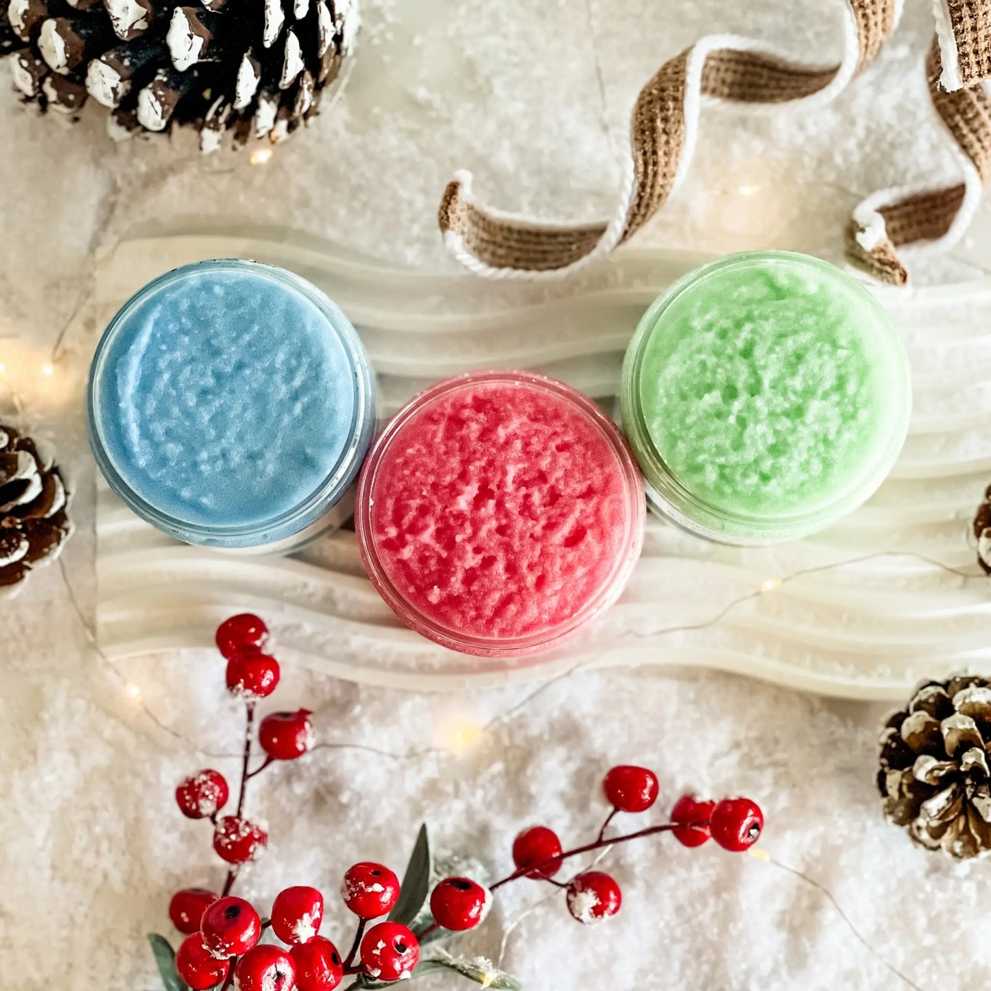 Three small jars of colored powder on a textured surface with pine cones and berries.