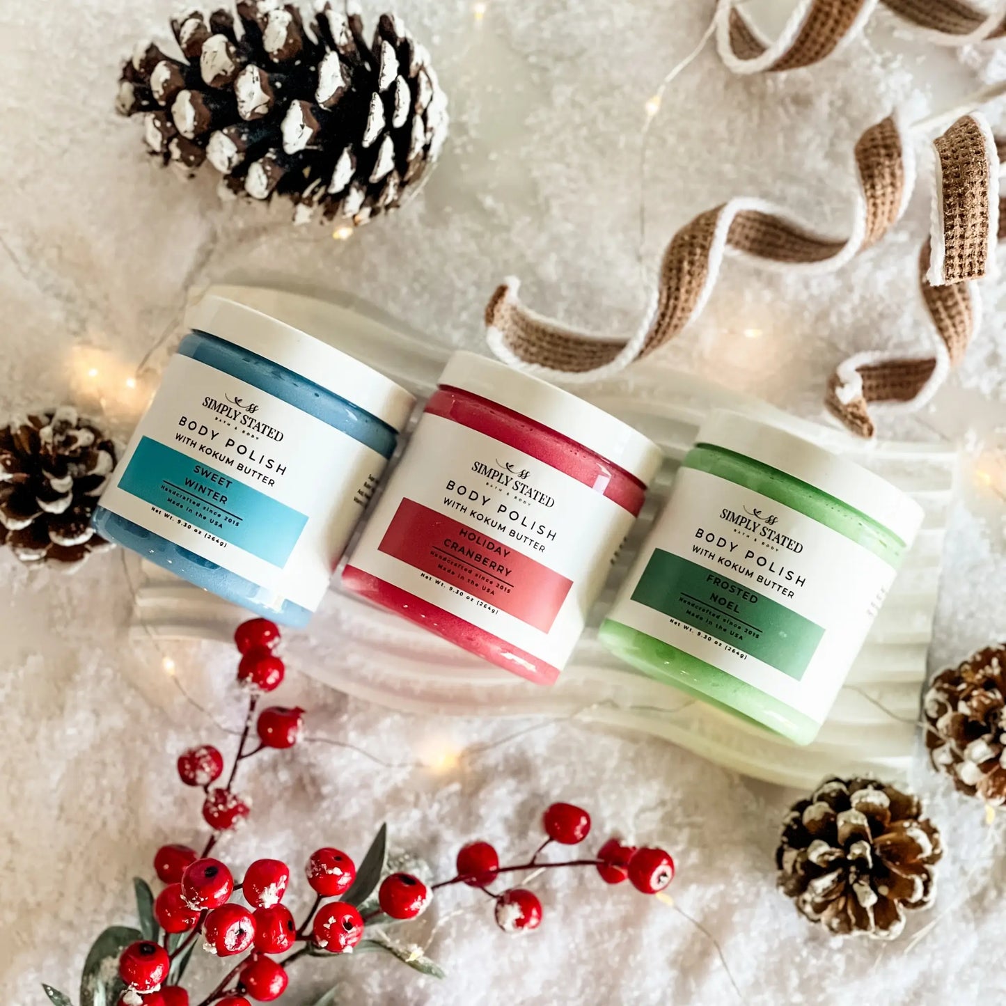 Three containers of body polish with decorative elements on a textured surface.