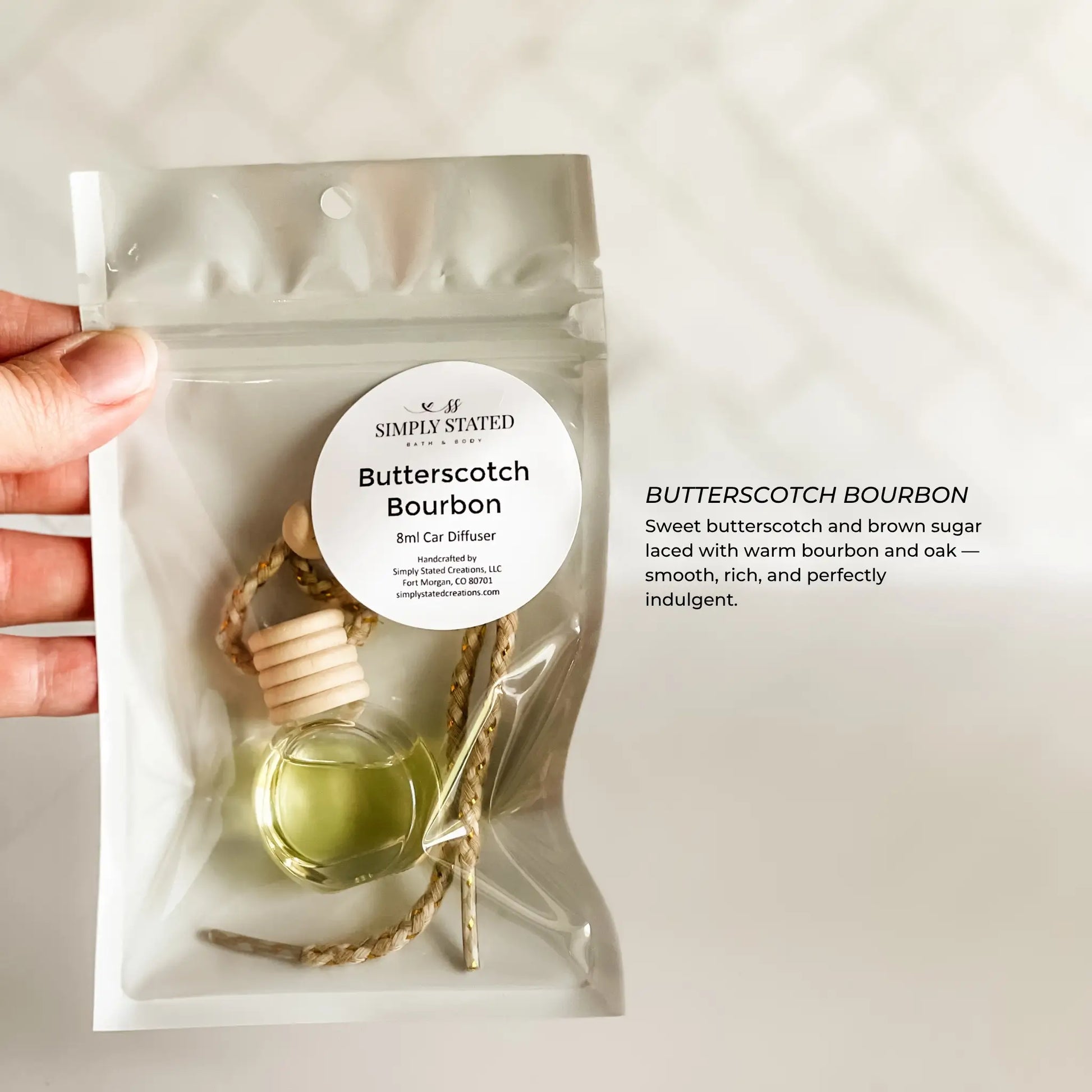 Car diffuser with 'Butterscotch Bourbon' fragrance held by a hand on a light background