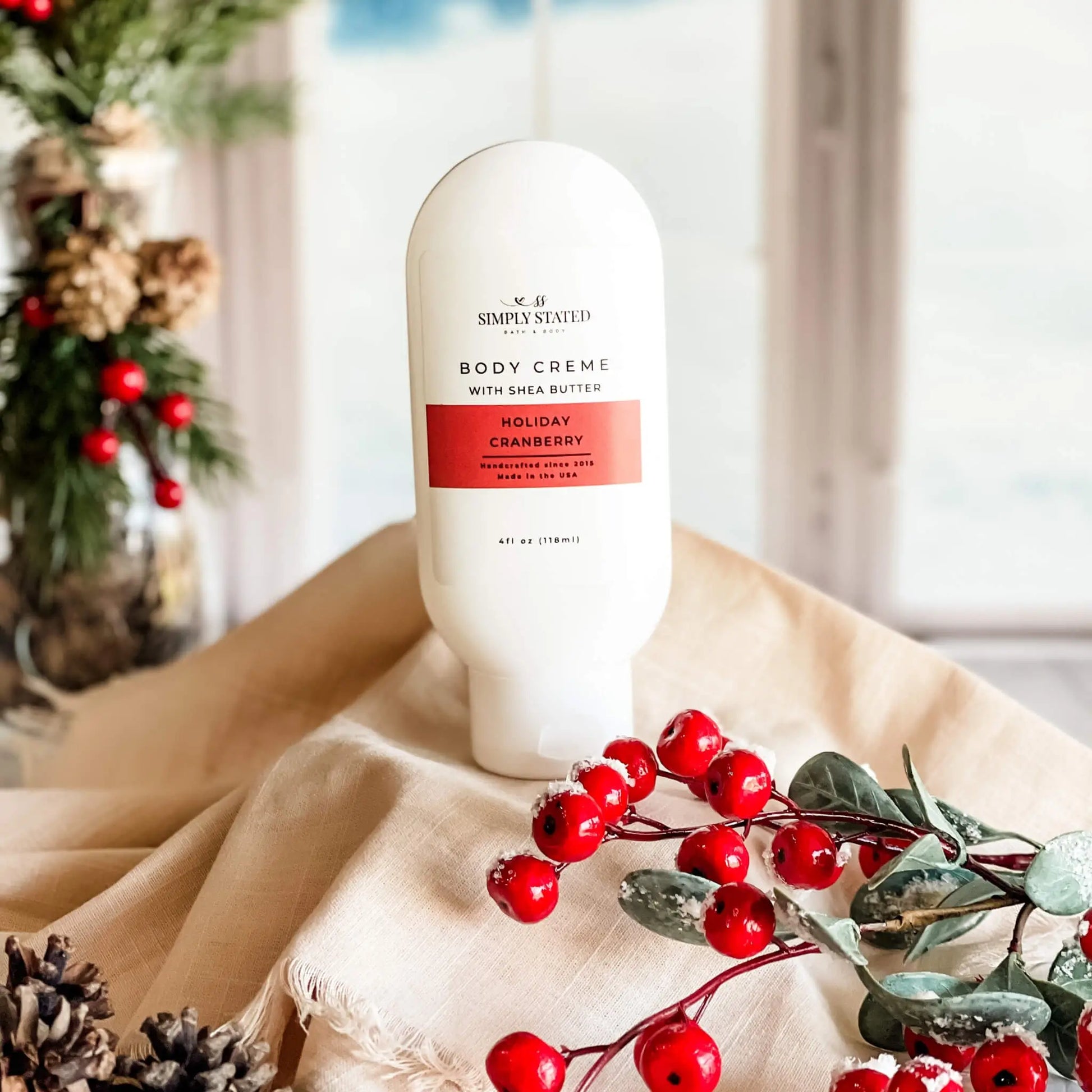 Body cream bottle with holiday cranberry design on a beige surface with decorative elements.